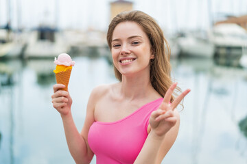 Canvas Print - Young redhead woman with a cornet ice cream at outdoors smiling and showing victory sign