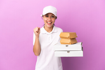 Wall Mural - Pizza delivery Russian girl with work uniform picking up pizza boxes and burgers isolated on purple background celebrating a victory in winner position