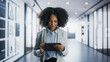 © Gorodenkoff - Portrait of a Young Empowered Black Female Business Manager Working on a Tablet Computer in a Modern Office Building. Confident African Specialist Looking Up Documents Online And Smiling In the Hall
