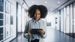 © Gorodenkoff - Portrait of Young Empowered Black Female Business Manager Working on a Tablet Computer in a Modern Office Building. Confident African Specialist Looking Up Documents Online And Smiling In the Hall