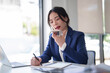 © Pichsakul - Businesswomen using smartphone to call with customer about financial and investment data of new business and taking notes while working to analysis strategy about new startup project in workplace
