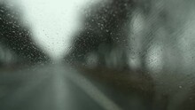 Close-up POV from inside a car onto raindrops on the windshield. Traveling along a snowy road on a rainy spring or winter day. First person view car passenger. Wipers wipe the windshield
