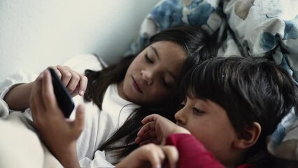 Wall Mural - Brother and Sister Engrossed in Smartphone Screen While Lying in Bed, Siblings Bonding Over Digital Device