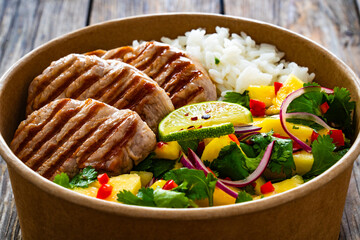 Poster - Grilled pork loin steaks with rice and mango salad in lunch box to go on wooden table
