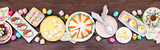 Fototapeta Uliczki - Easter or spring dessert food table scene. Above view over a dark wood banner background. Lemon tart, cupcakes, Easter egg and carrot cakes and various sweets.
