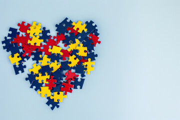 Wall Mural - Heart made from blue, yellow, red puzzles on light blue background. World autism awareness day concept. Top view, copy space