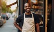 Portrait of happy African-American man small business owner of coffee shop standing at entrance wearing beige apron and black shirt