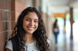 © Sascha - Contented teenage girl with curly hair and a genuine smile stands in a brick-walled school corridor, her demeanor relaxed and friendly.