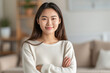 © Sascha - Smiling young Asian woman with crossed arms, radiating confidence and contentment in a cozy living room.