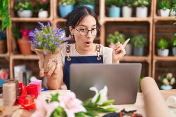 Canvas Print - Young hispanic woman working at florist shop doing video call surprised pointing with finger to the side, open mouth amazed expression.