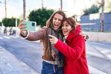 Wall Mural - Two women mother and daughter make selfie by smartphone at street