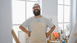 © Krakenimages.com - Handsome hispanic man with beard wearing apron in a bright art studio interior, smiling confidently at the camera.