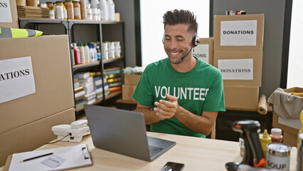 Wall Mural - Young, attractive hispanic man, clapping in applause, volunteers his computer skills at a charity center, while sitting and listening through headphones.