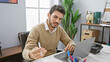 © Krakenimages.com - A handsome young hispanic man with a beard works diligently on his laptop in a modern office setting.