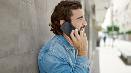 Young hispanic man talking on smartphone with serious expression at street