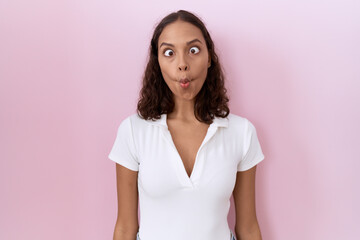 Wall Mural - Young hispanic woman wearing casual white t shirt making fish face with lips, crazy and comical gesture. funny expression.