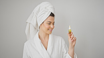 Poster - Young beautiful hispanic woman wearing bathrobe holding serum bottle over isolated white background