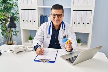 Poster - Young latin man doctor writing on document holding pills at clinic