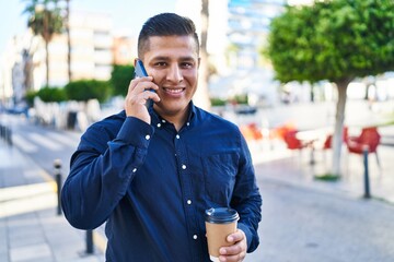 Sticker - Young latin man talking on smartphone drinking coffee at coffee shop terrace