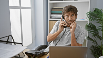 Poster - A handsome hispanic man with a beard and green eyes makes a phone call in a modern office interior.