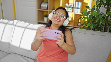 Poster - Young chinese woman watching video on smartphone sitting on sofa at home