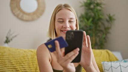 Wall Mural - Young blonde woman shopping with smartphone and credit card sitting on sofa at home