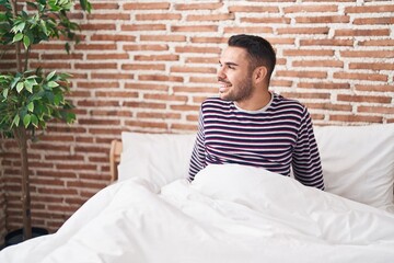 Poster - Young hispanic man smiling confident sitting on bed at bedroom