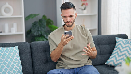 Canvas Print - Young hispanic man using smartphone sitting on sofa at home