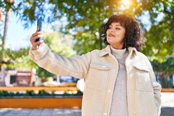 Wall Mural - Young beautiful hispanic woman smiling confident making selfie by the smartphone at park