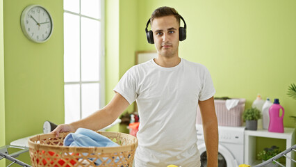 Wall Mural - A young man in headphones holding a laundry basket stands in a brightly lit home laundry room.