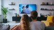 © Zahid - Back view of young family, man and woman watching TV together in living room, TV on white background