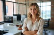 © LifeMedia - A confident woman exudes professionalism as she stands with arms crossed in her stylish office, surrounded by modern furniture and natural light pouring in from the large windows