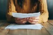 © tonstock - In a cozy sweater, a person thoughtfully reviews documents, the soft texture contrasting with the stark papers.