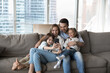 © fizkes - Parents with kids having fun at modern home resting on cozy sofa look at smartphone screen, watch cartoons, new video vlog spend time on internet in living room on weekend. Technology, family pastime
