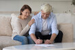 © fizkes - Positive senior retired husband and wife signing document, medical insurance agreement, investment contract, buying real estate property, bank papers, reviewing domestic bills