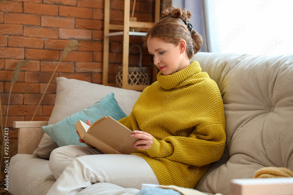 Young woman reading book on couch at home
