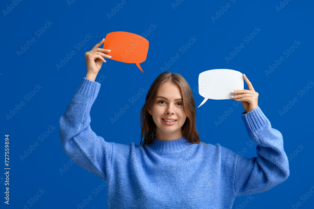Pretty young woman holding blank speech bubbles on blue background