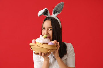 Poster - Pretty young woman with bunny ears and Easter basket on red background