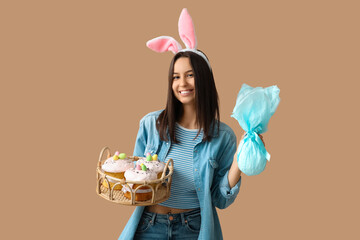 Poster - Pretty young woman with bunny ears, Easter basket and gift on beige background