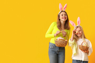 Poster - Cute little girl and her mother in bunny ears holding baskets of Easter cake with painted eggs on yellow background