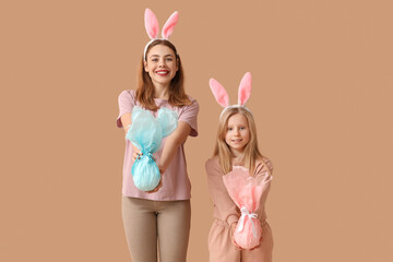 Poster - Cute little girl and her mother in bunny ears with Easter gift eggs on brown background