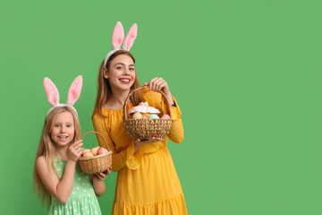 Poster - Cute little girl and her mother in bunny ears holding baskets of Easter cake with painted eggs on green background