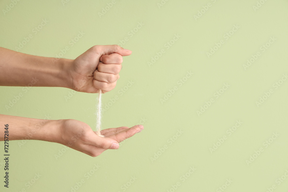 Male hands with pouring sand on green background. Time concept