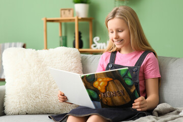 Sticker - Little girl reading book while sitting on sofa at home