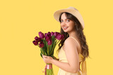 Fototapeta Tulipany - Happy young woman with bouquet of beautiful purple tulips on yellow background