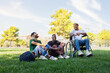 © Daniel - Young Black man in a wheelchair and friends laughing and having fun sitting on the grass in a park. Copy space.