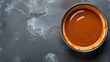 Smooth caramel sauce in a bowl, placed on a textured grey surface