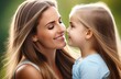 © Anastasia - A young mother and a little daughter look at each other and smile, they have long hair and summer clothes, blurred green background, closeup