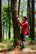 © Slaf - Javanese man in red is leaning against a tree in the forest.