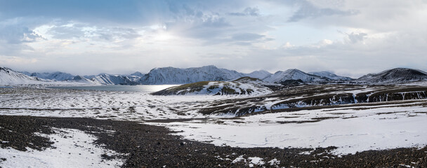 Wall Mural - Season changing in southern Highlands of Iceland. Colorful Landmannalaugar mountains under snow cover in autumn. Frostastadavatn lake at the foot of the mountains.